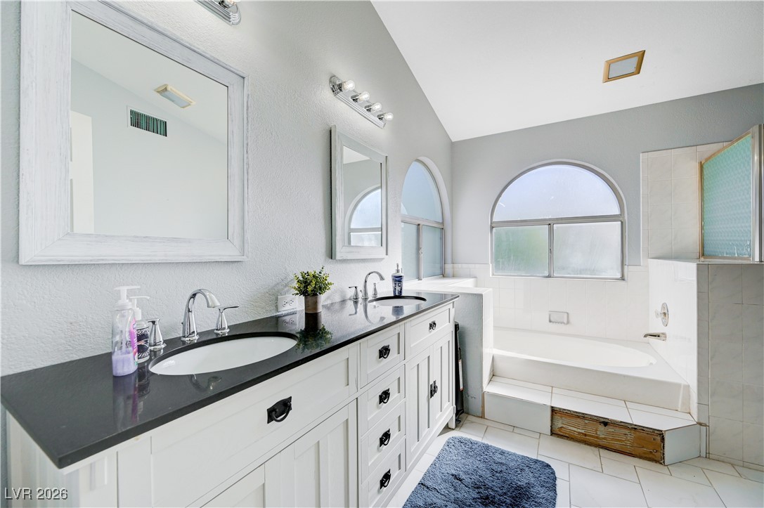 14 Barton Spring Circle Henderson, NV 89074 - Photo 32 of 64 Bathroom featuring lofted ceiling, double vanity, a garden tub, a textured wall, and light tile patterned floors