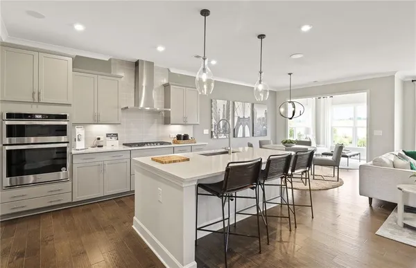 a kitchen with stainless steel appliances granite countertop a stove a sink a refrigerator a dining table and chairs with wooden floor
