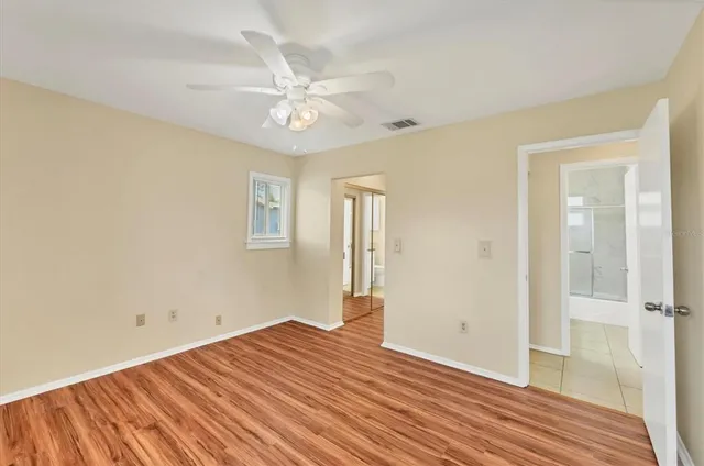 an empty room with wooden floor fan and windows