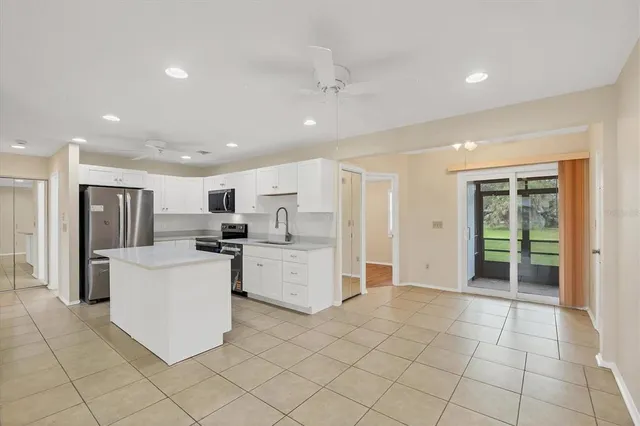 a large white kitchen with stainless steel appliances granite countertop a couch and a view of living room