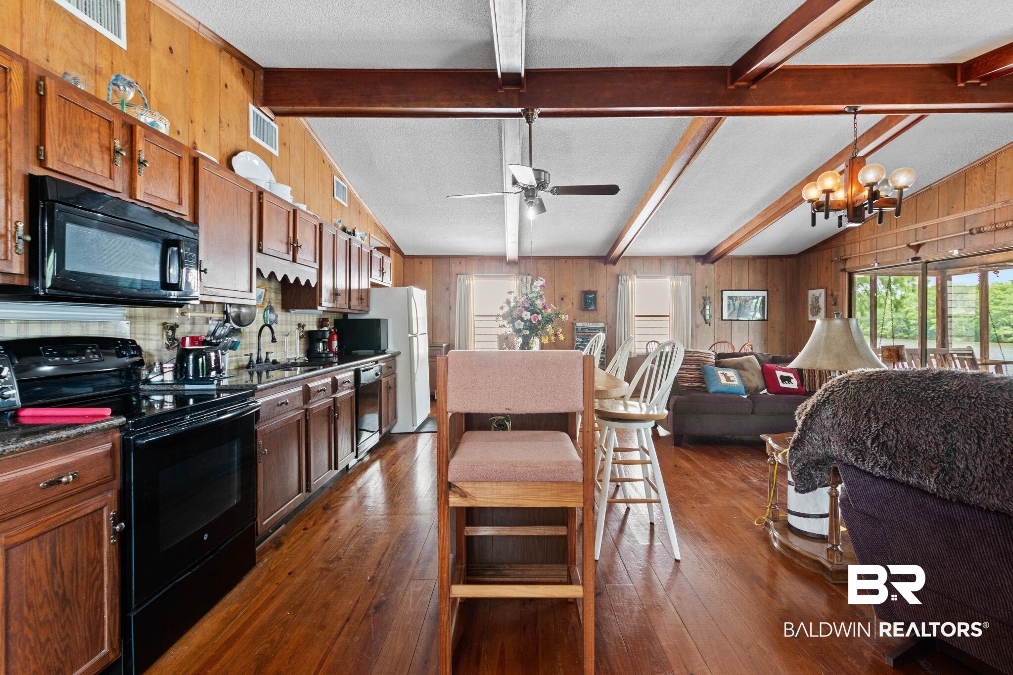 8153 Bryant's Lndg Road Stockton, AL 36579 - Photo 23 of 87 Open-concept kitchen and living area featuring wood-finish flooring, exposed ceiling beams, wood paneling, and built-in cabinetry