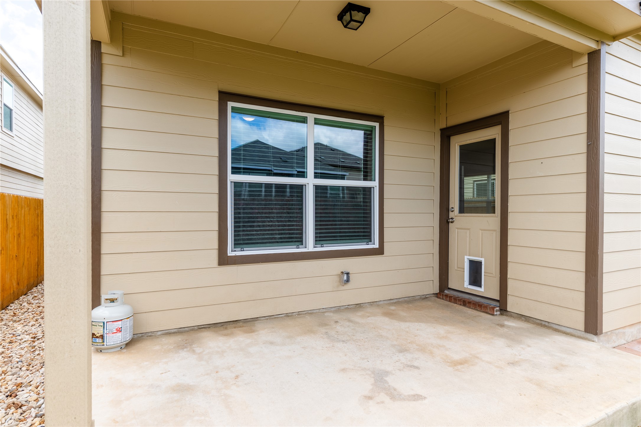 425 Perfect World Loop Jarrell, TX 76537 - Photo 25 of 29 Covered patio featuring a concrete slab, beige siding, white window trim, brown door trim, and an exterior light fixture