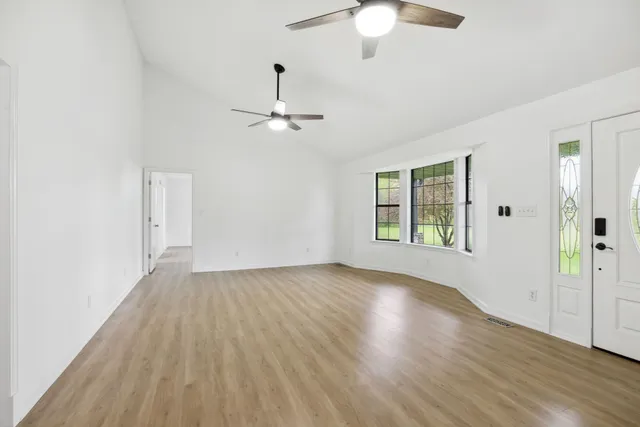 an empty room with wooden floor chandelier fan and windows