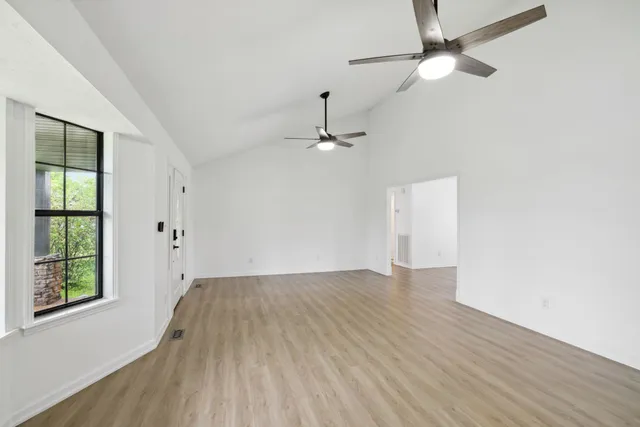 an empty room with wooden floor chandelier fan and windows