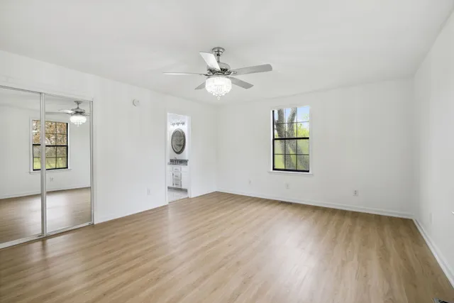 an empty room with wooden floor chandelier fan and windows