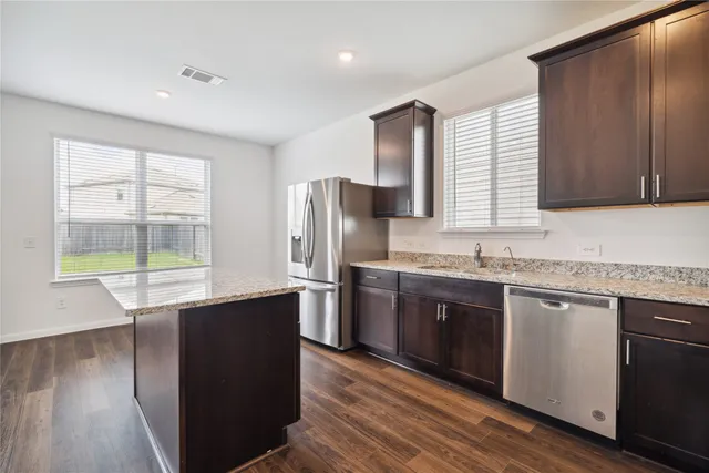 a kitchen with stainless steel appliances granite countertop a sink a stove a refrigerator and island with wooden floor