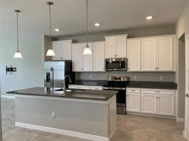 a kitchen with kitchen island granite countertop a stove a sink a refrigerator and white cabinets with wooden floor