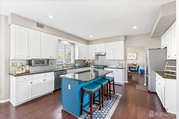 a kitchen with stainless steel appliances granite countertop a refrigerator a sink dishwasher a stove and white countertops with wooden floor