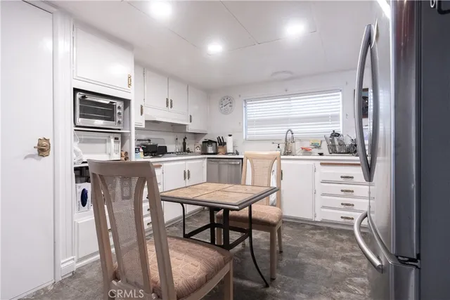 a kitchen with stainless steel appliances a dining table chairs refrigerator and sink