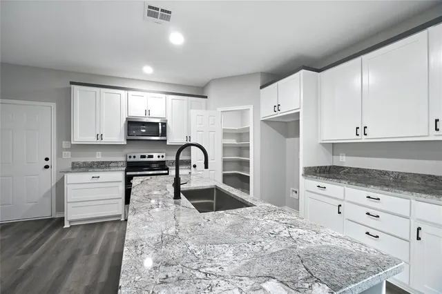 a kitchen with granite countertop white cabinets and stainless steel appliances