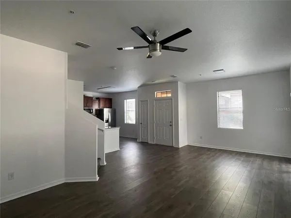 an empty room with wooden floor a ceiling fan and windows