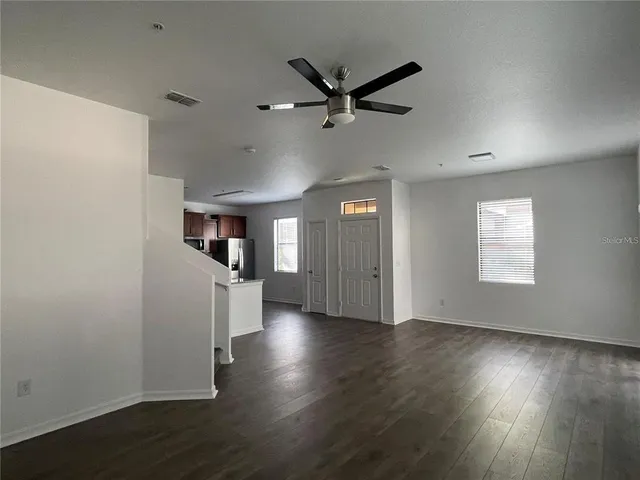 an empty room with wooden floor a ceiling fan and windows