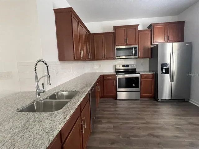 a kitchen with stainless steel appliances granite countertop a sink a stove a refrigerator with wooden cabinets