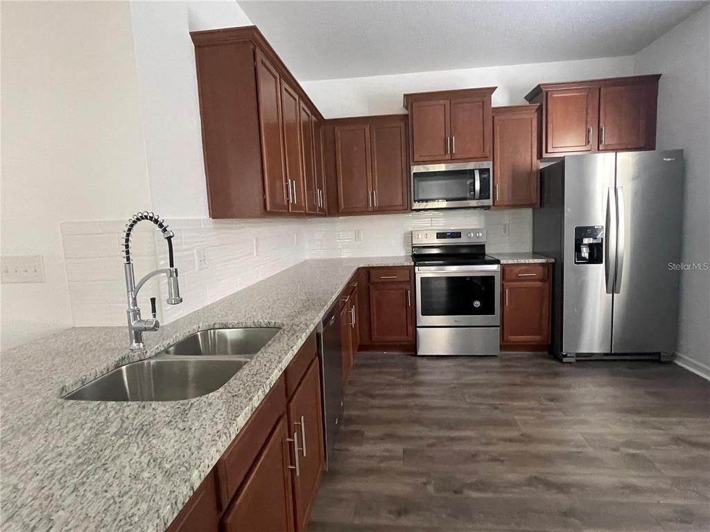 3739 Seneca Club Loop, Unit A Orlando, FL 32808 - Photo 6 of 31 a kitchen with stainless steel appliances granite countertop a sink a stove a refrigerator with wooden cabinets