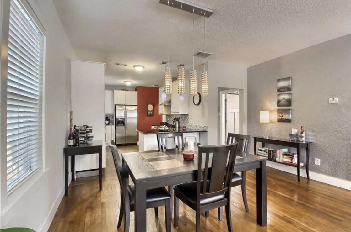 702 West N Loop Boulevard Austin, TX 78751 - Photo 14 of 23 Hardwood floors flow through this welcoming dining area, illuminated by stylish pendant lighting, opening to a modern kitchen.