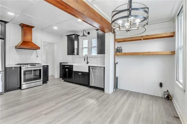 a view of a kitchen with stainless steel appliances granite countertop a stove top oven a chimney wooden floor and cabinets