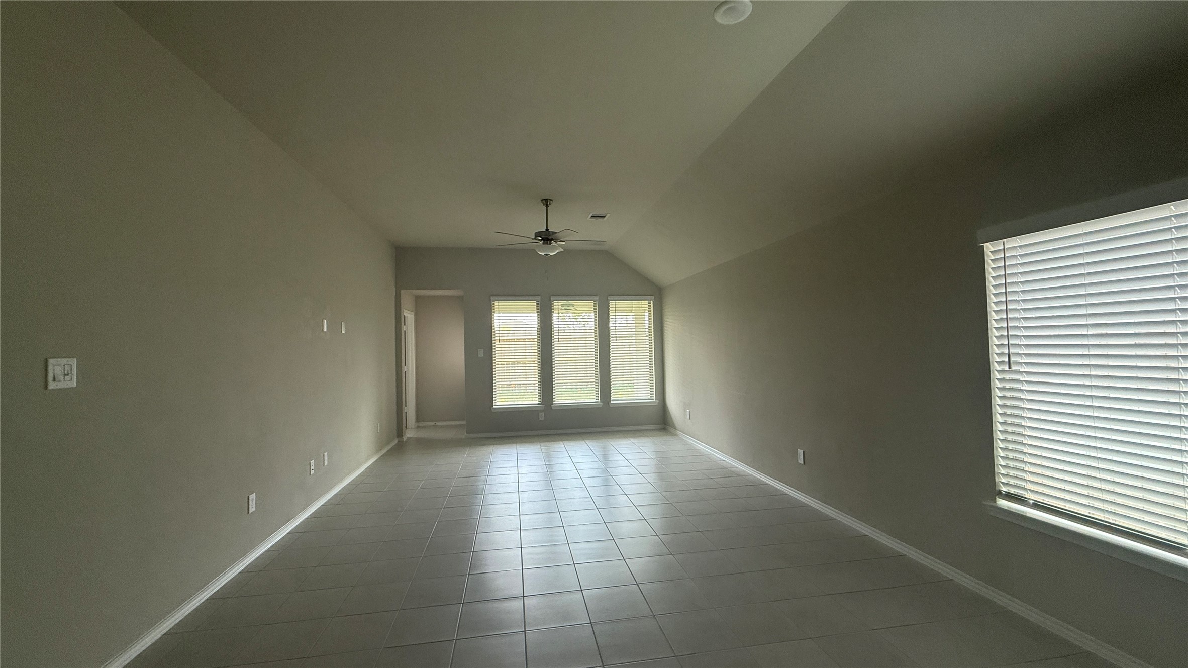 31961 Retama Rnch Drive Spring, TX 77386 - Photo 17 of 25 This photo showcases a spacious, empty room with tiled flooring, neutral walls, and large windows allowing natural light. A ceiling fan is centrally located, and the room has a high, sloping ceiling, giving it an airy feel.