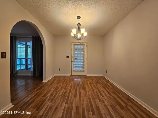 an empty room with wooden floor chandelier and windows