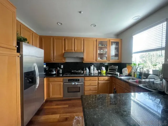 a kitchen with stainless steel appliances granite countertop a stove a sink dishwasher a refrigerator white cabinets and wooden floor