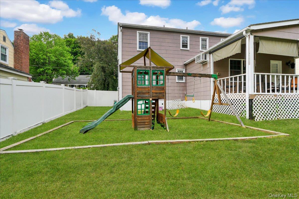 10 Susquehanna Road Ossining, NY 10562 - Photo 21 of 31 Expansive green lawn featuring a wooden playset with slide and swings, a white privacy fence, and a covered porch with white lattice skirting
