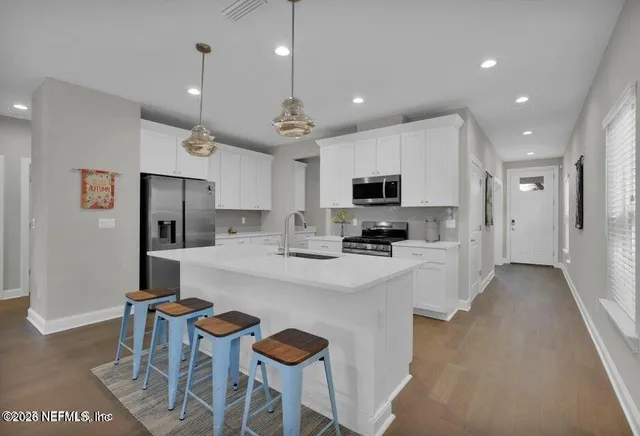 a kitchen with stainless steel appliances kitchen island granite countertop a stove a refrigerator a oven a sink a dining table and chairs with wooden floor
