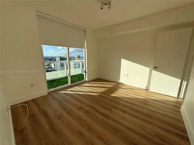 a view of an empty room with wooden floor and a window