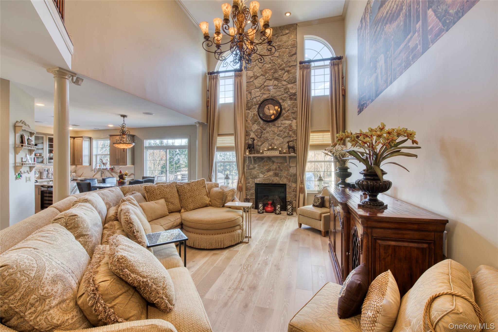395 Stonecrop Road Riverhead, NY 11901 - Photo 11 of 38 Living room featuring a high ceiling, oak wood floors, plenty of natural light, ornamental molding, and a stone fireplace