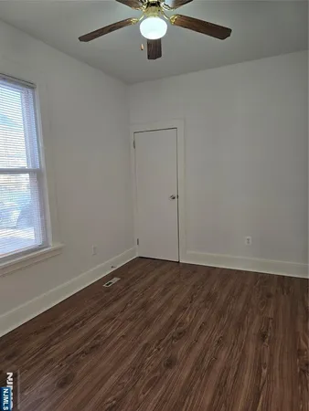 an empty room with wooden floor fan and windows