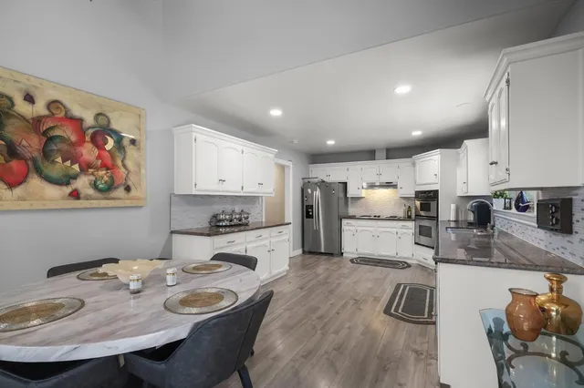 a large kitchen with kitchen island a stove a sink a refrigerator and white cabinets with wooden floor