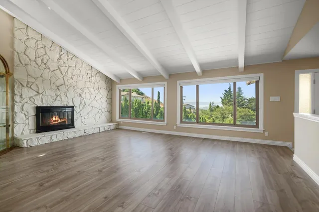 an empty room with wooden floor fireplace and windows