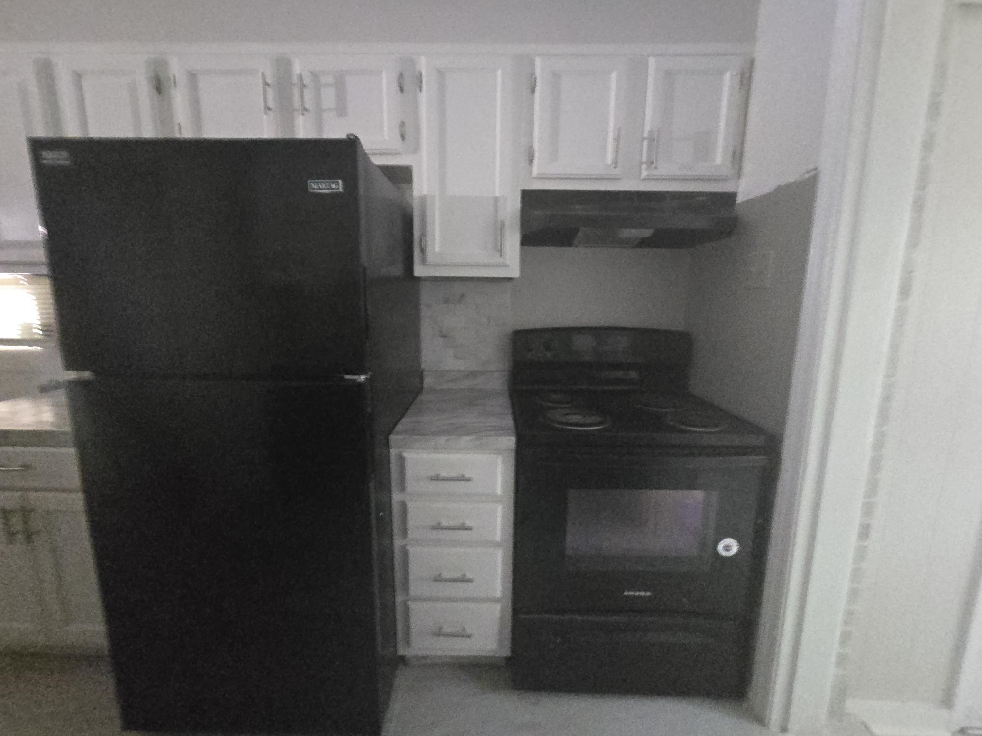 Kitchen featuring black appliances, ventilation hood, white cabinets, and light countertops