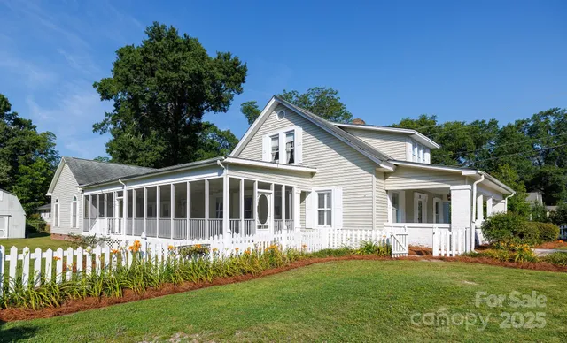 a view of a white house with a small yard and large trees