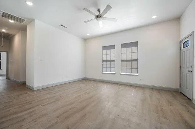 an empty room with wooden floor chandelier fan and windows