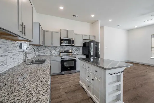 a kitchen with stainless steel appliances granite countertop a stove top oven a sink and a refrigerator