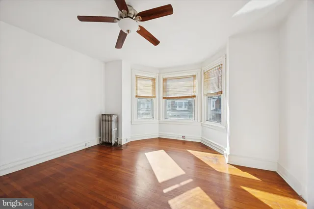 an empty room with wooden floor fan and windows