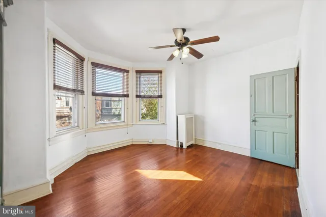 an empty room with wooden floor fan and windows