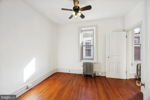 an empty room with wooden floor chandelier fan and windows