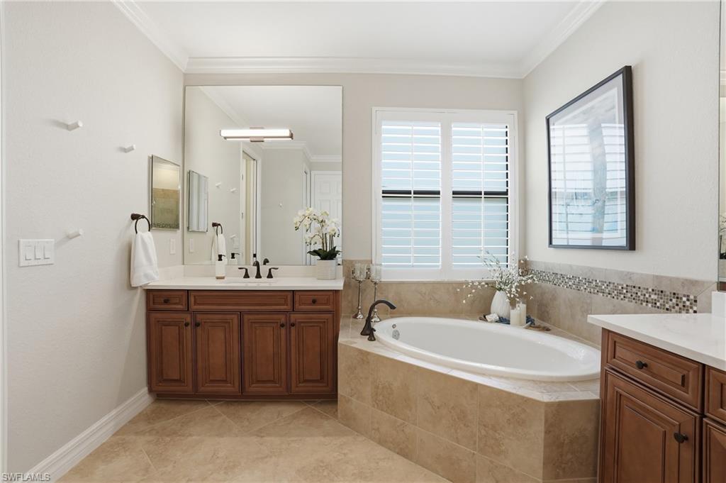 3058 Aviamar Circle Naples, FL 34114 - Photo 14 of 50 Bathroom featuring a built-in soaking tub with tiled surround, wood-finish vanity with countertop, and plantation shutters