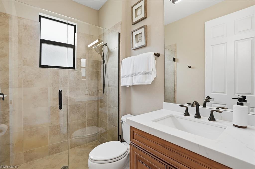 3058 Aviamar Circle Naples, FL 34114 - Photo 18 of 50 Bathroom featuring a glass-enclosed shower with tile surround, a built-in window, a vanity with a white countertop and integrated sink, and an oil-rubbed bronze faucet