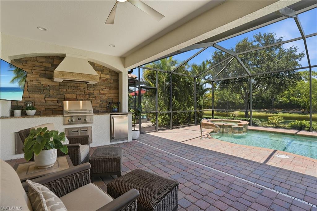 3058 Aviamar Circle Naples, FL 34114 - Photo 20 of 50 Screened outdoor living area featuring a built-in outdoor kitchen with a stone-accented wall, stainless steel grill, and refrigerator