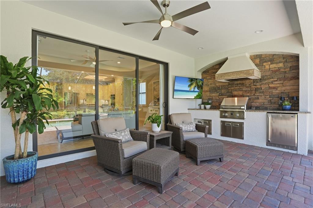 3058 Aviamar Circle Naples, FL 34114 - Photo 22 of 50 Covered outdoor living space featuring a built-in outdoor kitchen with stainless steel grill and refrigerator, stone-accented wall, and recessed lighting