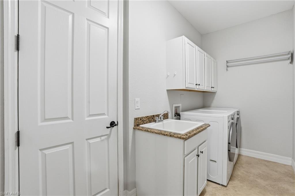 3058 Aviamar Circle Naples, FL 34114 - Photo 28 of 50 Functional utility room featuring a built-in sink with a granite-look countertop, white cabinetry with black hardware, and a wall-mounted drying rack