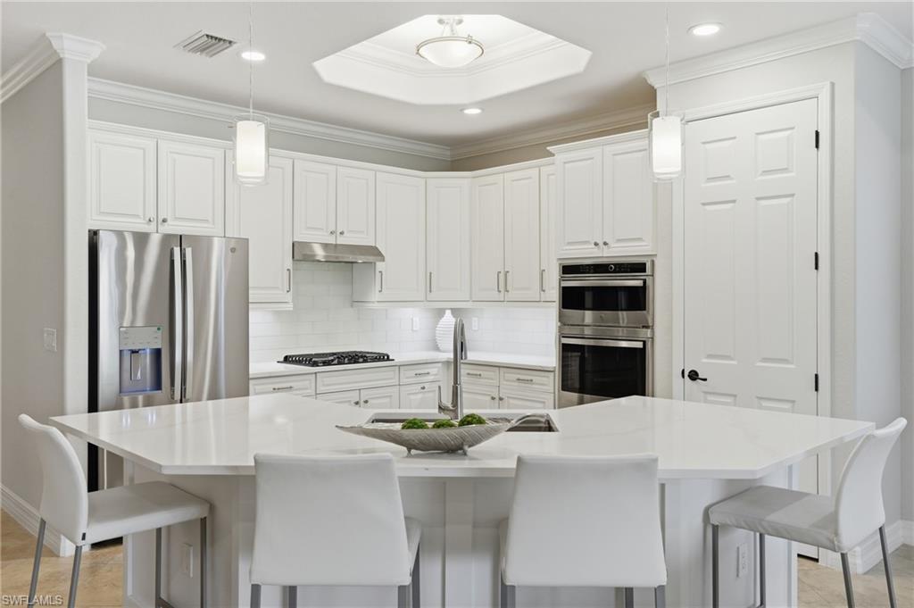 3058 Aviamar Circle Naples, FL 34114 - Photo 3 of 50 Spacious kitchen featuring an angular island with integrated sink, white cabinetry, stainless steel appliances, a tile backsplash, and recessed lighting