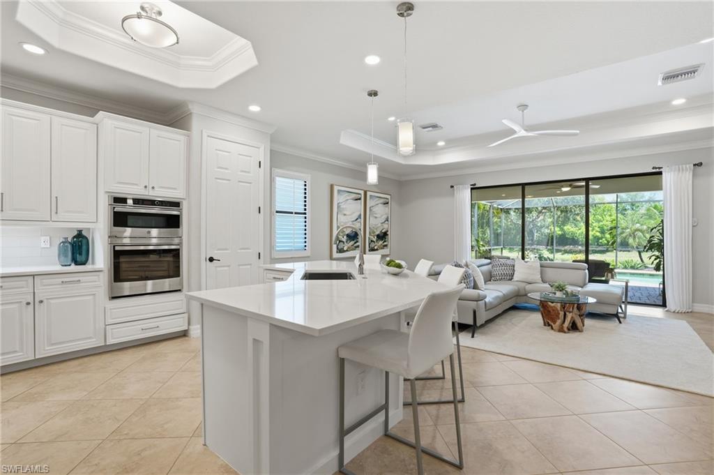 3058 Aviamar Circle Naples, FL 34114 - Photo 4 of 50 Open-concept living space featuring a central kitchen island with a white countertop, built-in stainless steel double ovens, and large sliding glass doors opening to the screened outdoor area