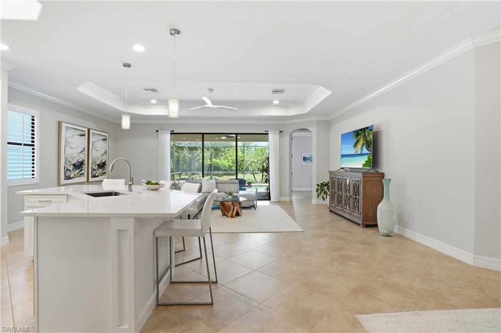 3058 Aviamar Circle Naples, FL 34114 - Photo 5 of 50 Open-concept living area featuring large format tile flooring, a kitchen island with integrated sink, pendant lighting, and a tray ceiling