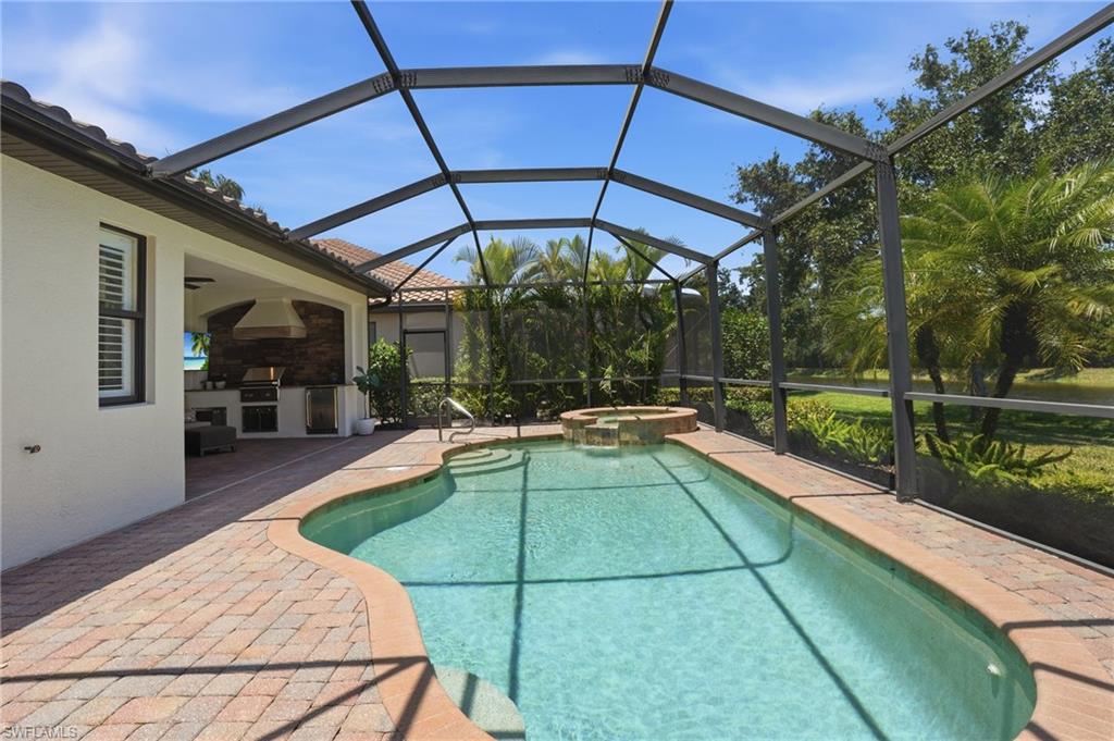 3058 Aviamar Circle Naples, FL 34114 - Photo 6 of 50 Screened outdoor living area featuring a custom-shaped pool with integrated spa, paver patio, full outdoor kitchen with built-in grill, and mature landscaping
