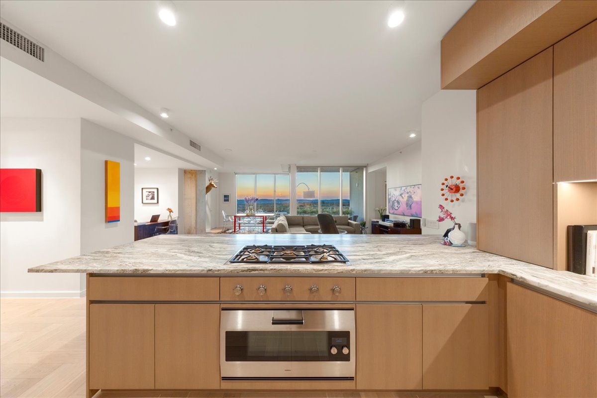 A custom kitchen designed for Omakase-style cooking, showcasing the Gaggenau® 5-burner gas cooktop and upgraded 36” oven with blue enamel interior. The 3cm Fantasy Brown marble counters extend across steel-reinforced overhangs that seat eight, creating an effortless connection to the dining and living areas. Floor-to-ceiling windows frame uninterrupted Hill Country and sunset views, making the entire space feel both intimate and expansive.