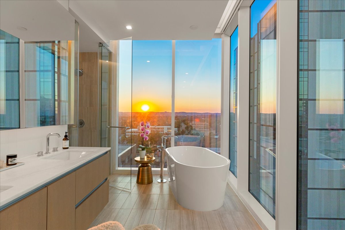 313 West 17th Street, Unit 1104 Austin, TX 78701 - Photo 4 of 40 Soak in luxury with breathtaking sunset views from this spa-inspired primary bath. A freestanding soaking tub is framed by floor-to-ceiling windows, while the floating double vanity features custom marble counters and modern cabinetry. A glass-enclosed walk-in shower completes the composition. This serene retreat blends elevated design with panoramic skyline and Hill Country vistas.