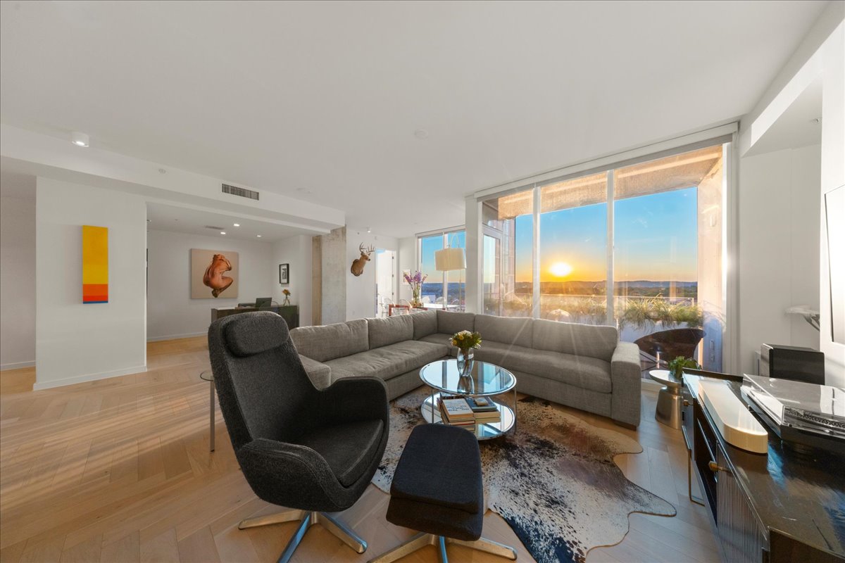 313 West 17th Street, Unit 1104 Austin, TX 78701 - Photo 8 of 40 A generous corner living room wrapped in floor-to-ceiling glass, offering uninterrupted Hill Country and sunset vistas. The upgraded herringbone wood floors and open, gallery-like layout create a warm, modern backdrop for both relaxed evenings and elevated entertaining.