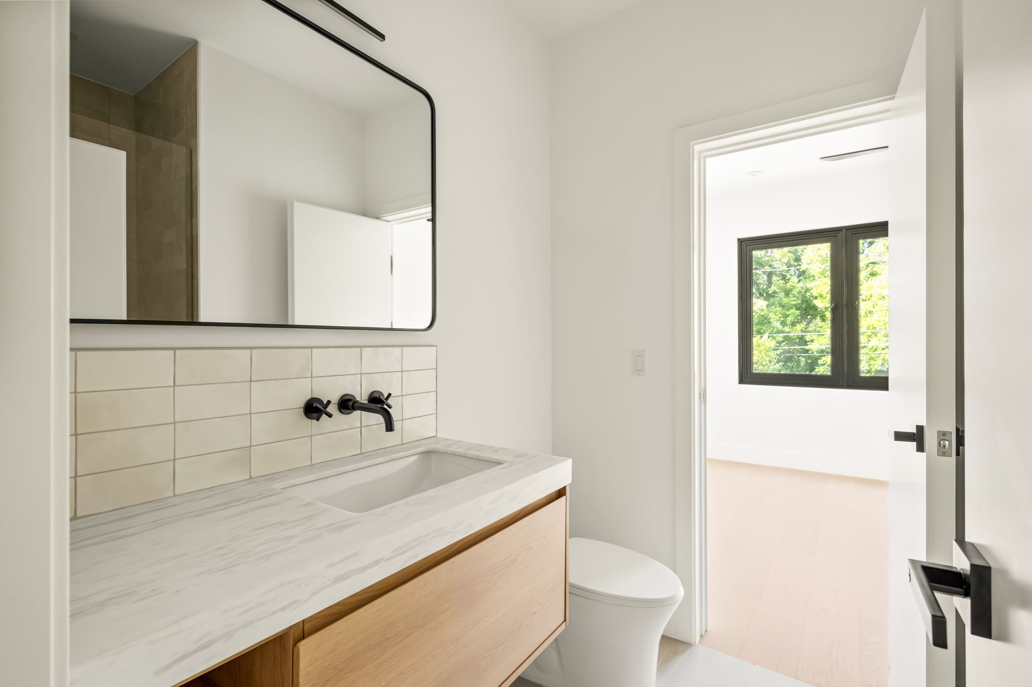 3210 Thompson Street Austin, TX 78702 - Photo 27 of 39 A modern bathroom features a sleek vanity with a rectangular mirror and a discreet toilet, offering a refined aesthetic.